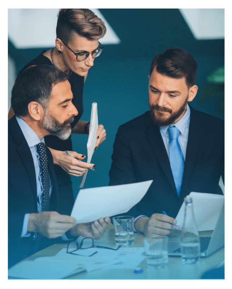 Three executives in a boardroom discussing printed documents and reports during a strategic planning meeting